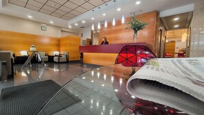 Zona de recepción de un hotel con diseño moderno, que incluye un mostrador de recepción, área de estar y un jarrón grande con plantas.