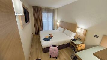 A hotel room with a bed, bedside tables, a lamp, a suitcase, and a TV mounted on the wall.
