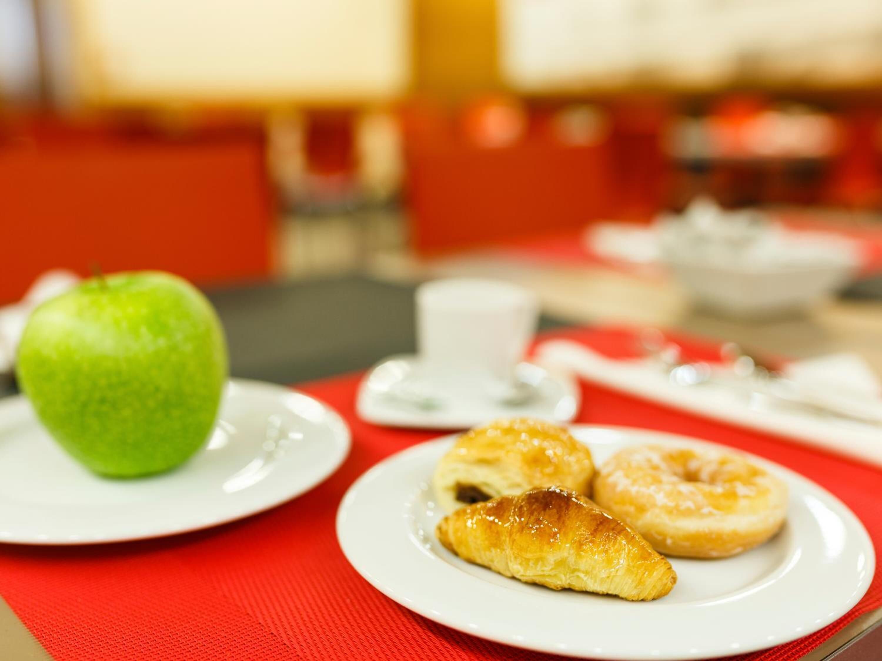 Un desayuno con una manzana verde, un croissant y una rosquilla sobre platos blancos.