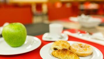 Un desayuno con una manzana verde, un croissant y una rosquilla sobre platos blancos.