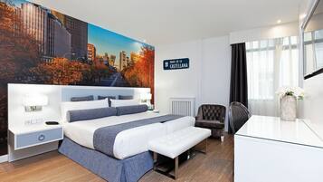 Una habitación de hotel moderna con una cama grande, mesitas de noche, un escritorio, una silla y un mural con vistas a la ciudad.