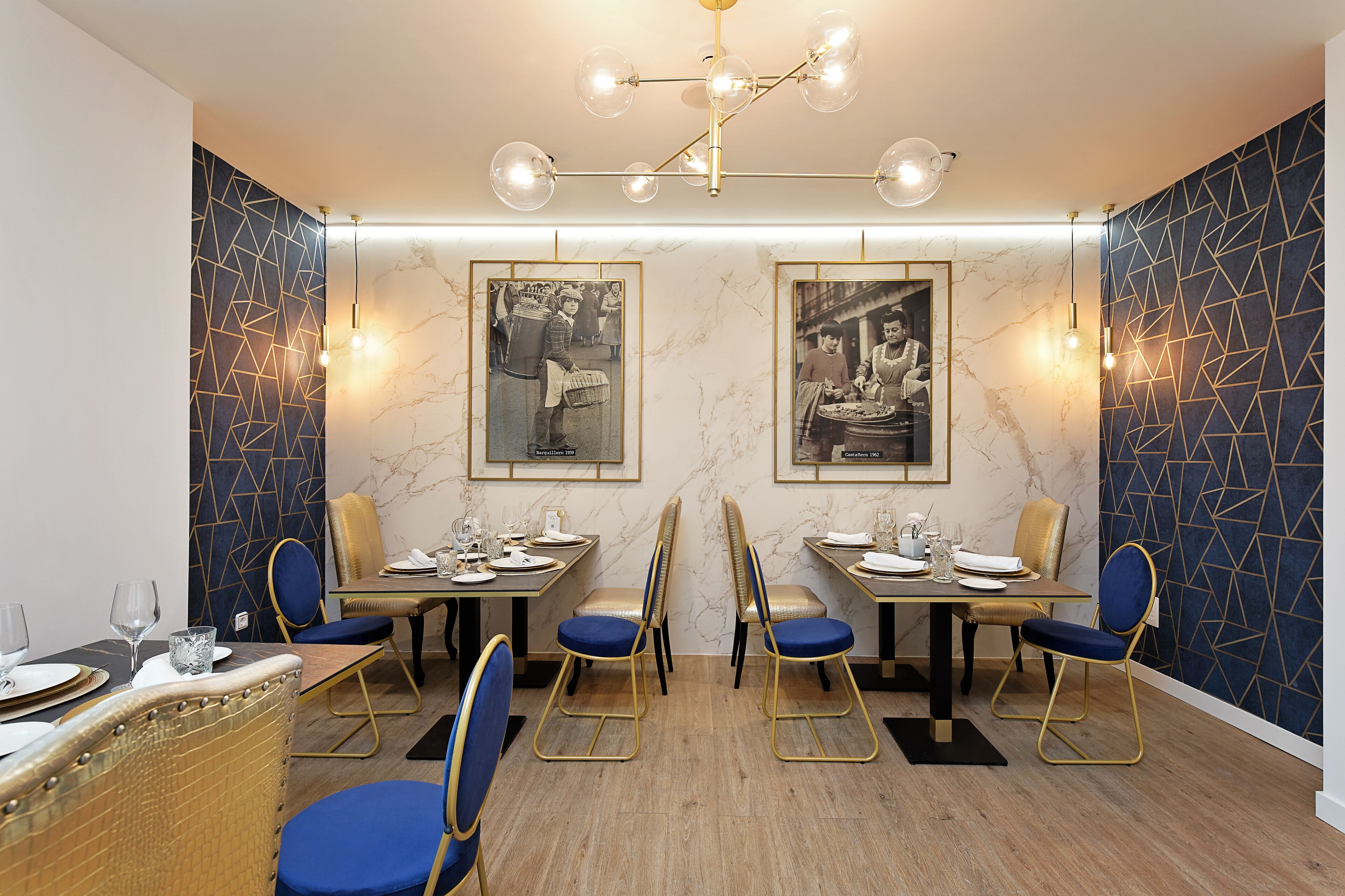 A dining area with tables set for four, blue chairs, and framed photographs on the walls.