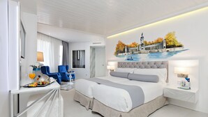 Een moderne hotelkamer met een groot bed, een bureau met stoel, een zithoek en een muurschildering van een historisch gebouw.