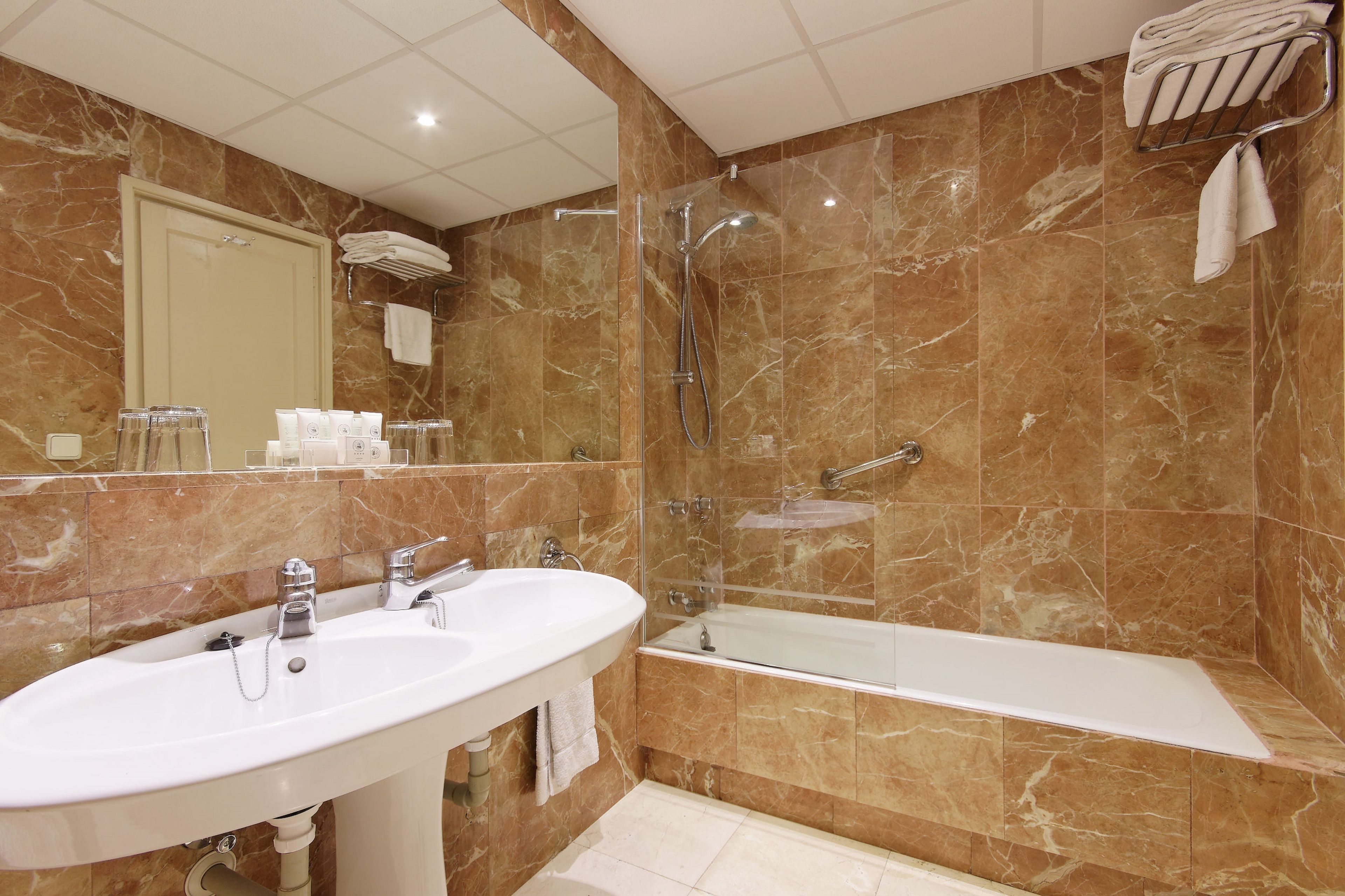 A bathroom with a marble wall, a sink, a bathtub, and a glass-enclosed shower.