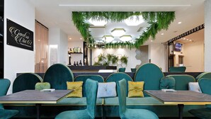 Een restaurantinterieur met smaragdgroene stoelen, een zwart en goudkleurig tafel en een hangende plantdecoratie.