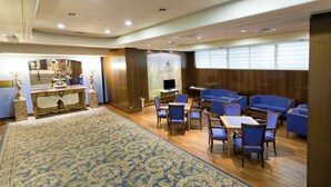 A hotel lobby with a blue patterned carpet, wooden flooring, a reception desk, and seating areas with blue upholstered chairs and tables. - Hotel Agumar Atocha (Madrid)