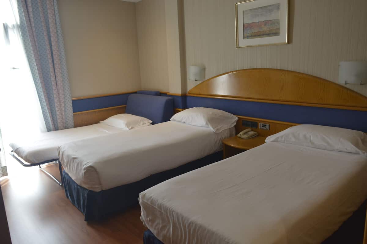 A hotel room with two single beds, a wooden headboard, a bedside table with a lamp, and a framed picture on the wall.