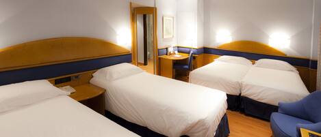 A hotel room with three single beds, a desk, and a chair.