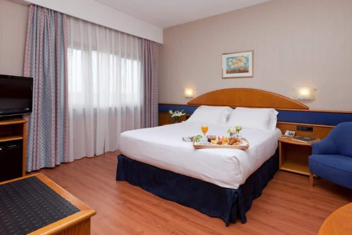 A hotel room with a bed, a TV, a desk, a chair, and a breakfast tray on the bed.