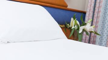 Una cama con ropa de cama blanca, cabecera de madera y un arreglo floral a un lado.