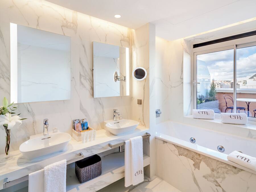 Un baño moderno con un espejo grande, dos lavamanos, una bañera y una ventana con vistas a la ciudad.