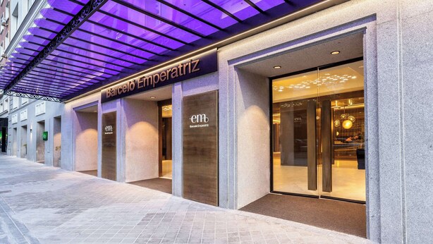 A modern hotel facade with a prominent entrance, large glass windows, and a purple-lit awning.