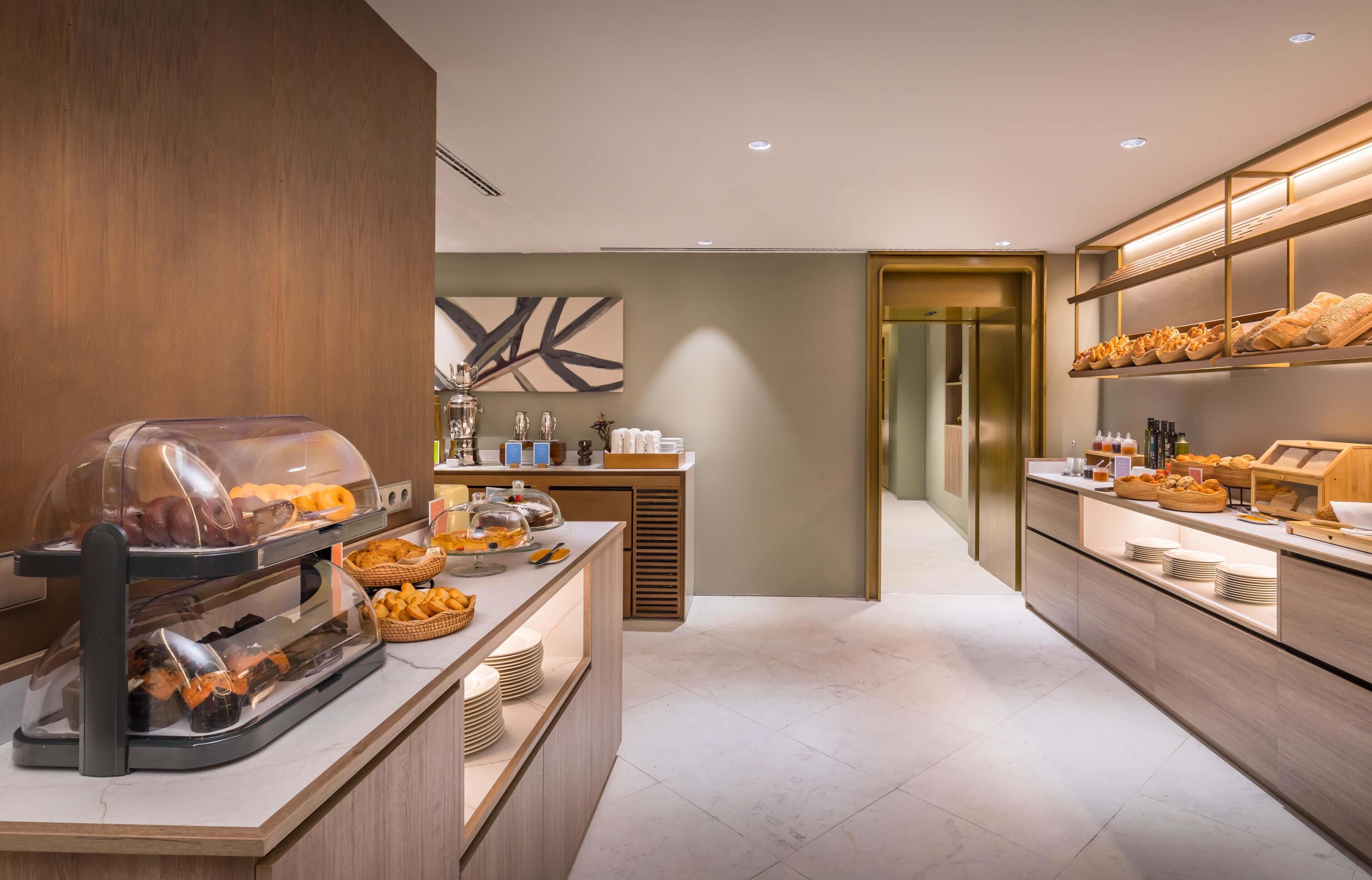 Un espace moderne dédié au petit-déjeuner dans l’hôtel, avec un buffet proposant du pain, des viennoiseries et un coin café.
