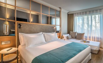 A hotel room with a large bed, a smaller sofa, a bedside table, and a mirror.