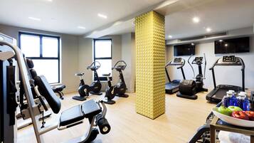 Un gimnasio con diferentes equipos de ejercicio, un pilar grande y una mesa con botellas de agua y manzanas.