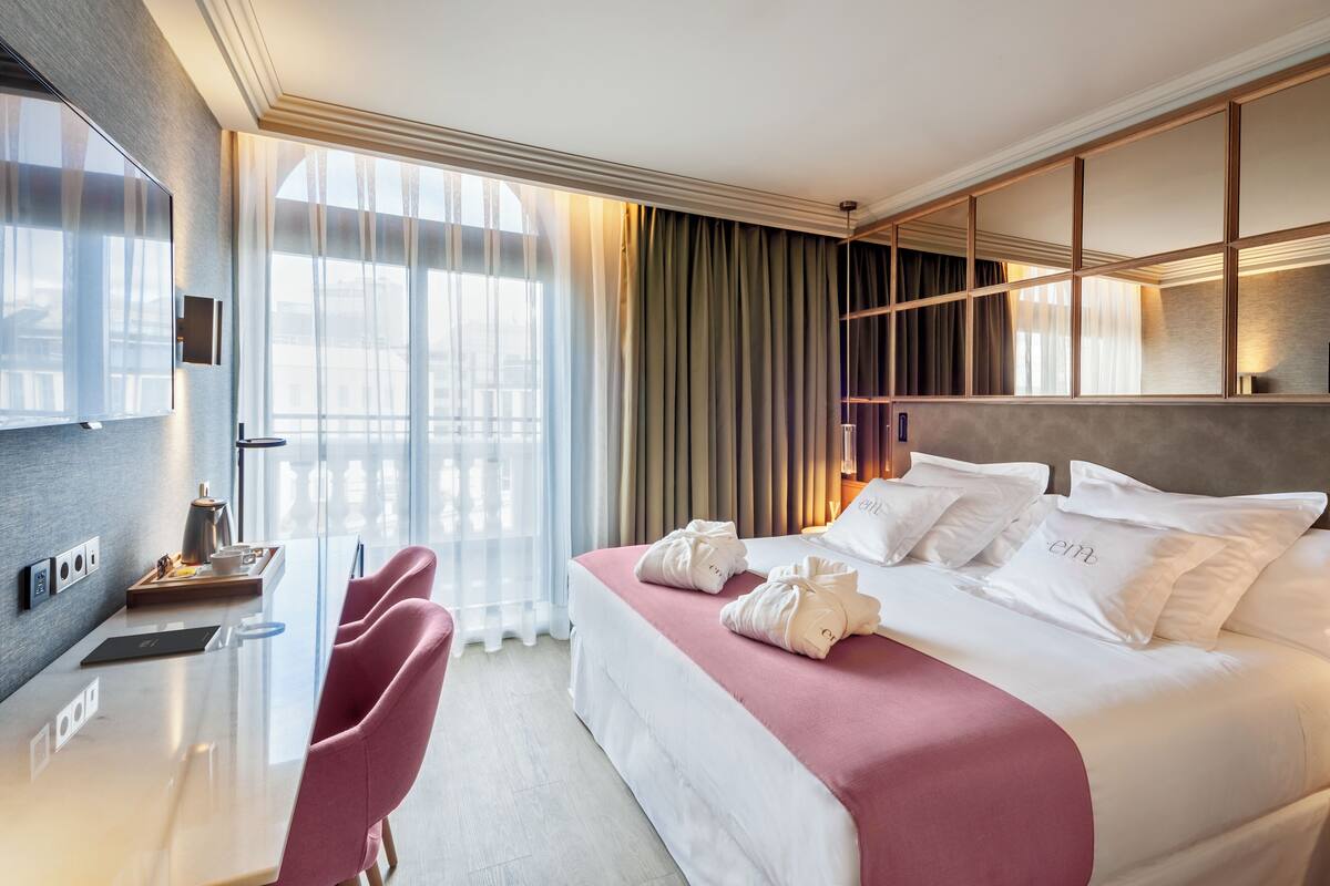 A modern hotel room with a large bed, a desk, and a view of the city.
