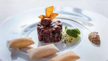 A plate with a dish of minced meat, garnished with a flower-like item, and surrounded by three spring rolls and a small salad.