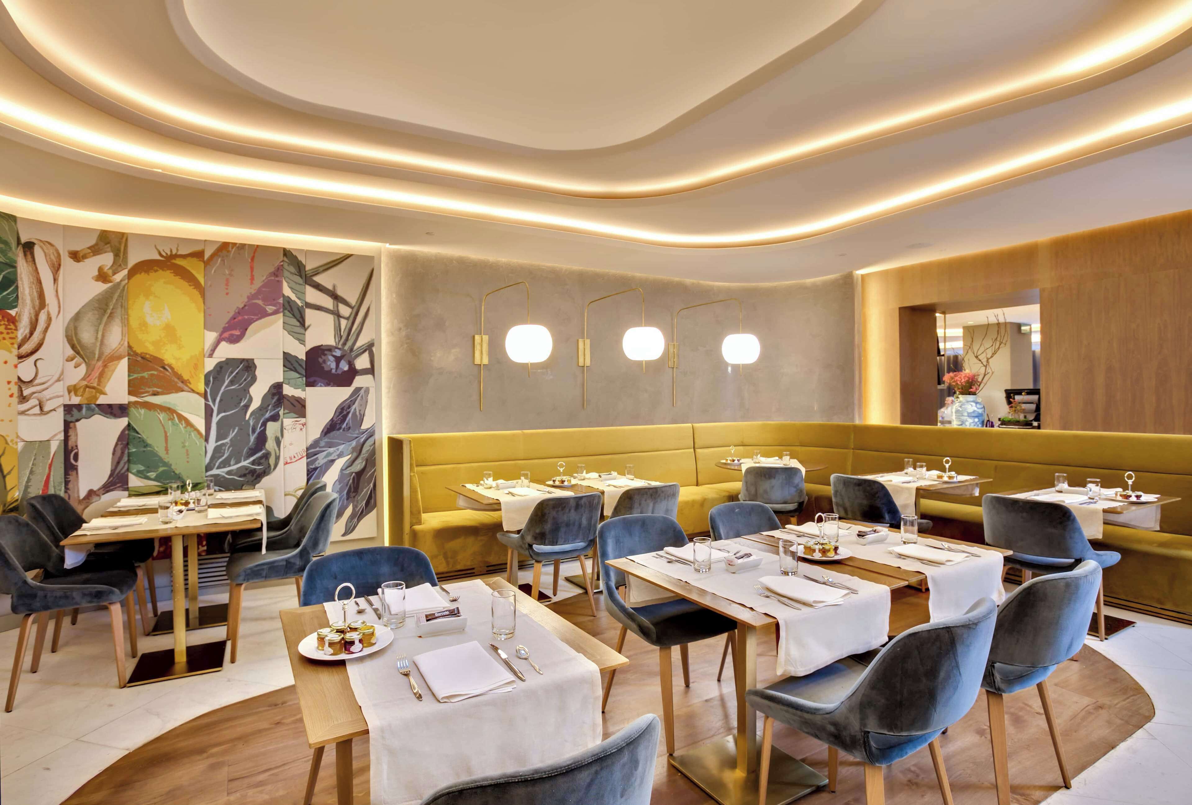 A modern restaurant with tables set for dining, a yellow accent wall, and contemporary lighting fixtures.