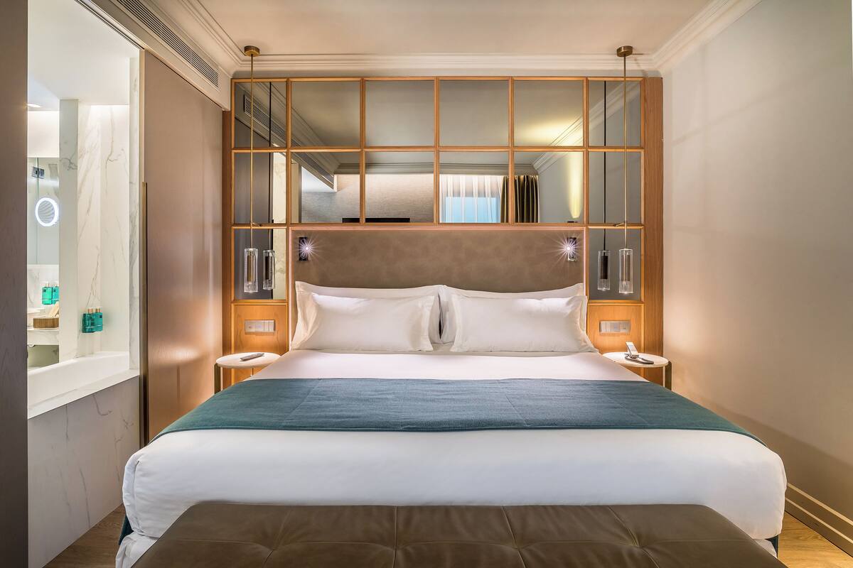 A hotel room with a large bed, a mirror with a wooden frame, bedside tables, and a view of the bathroom.