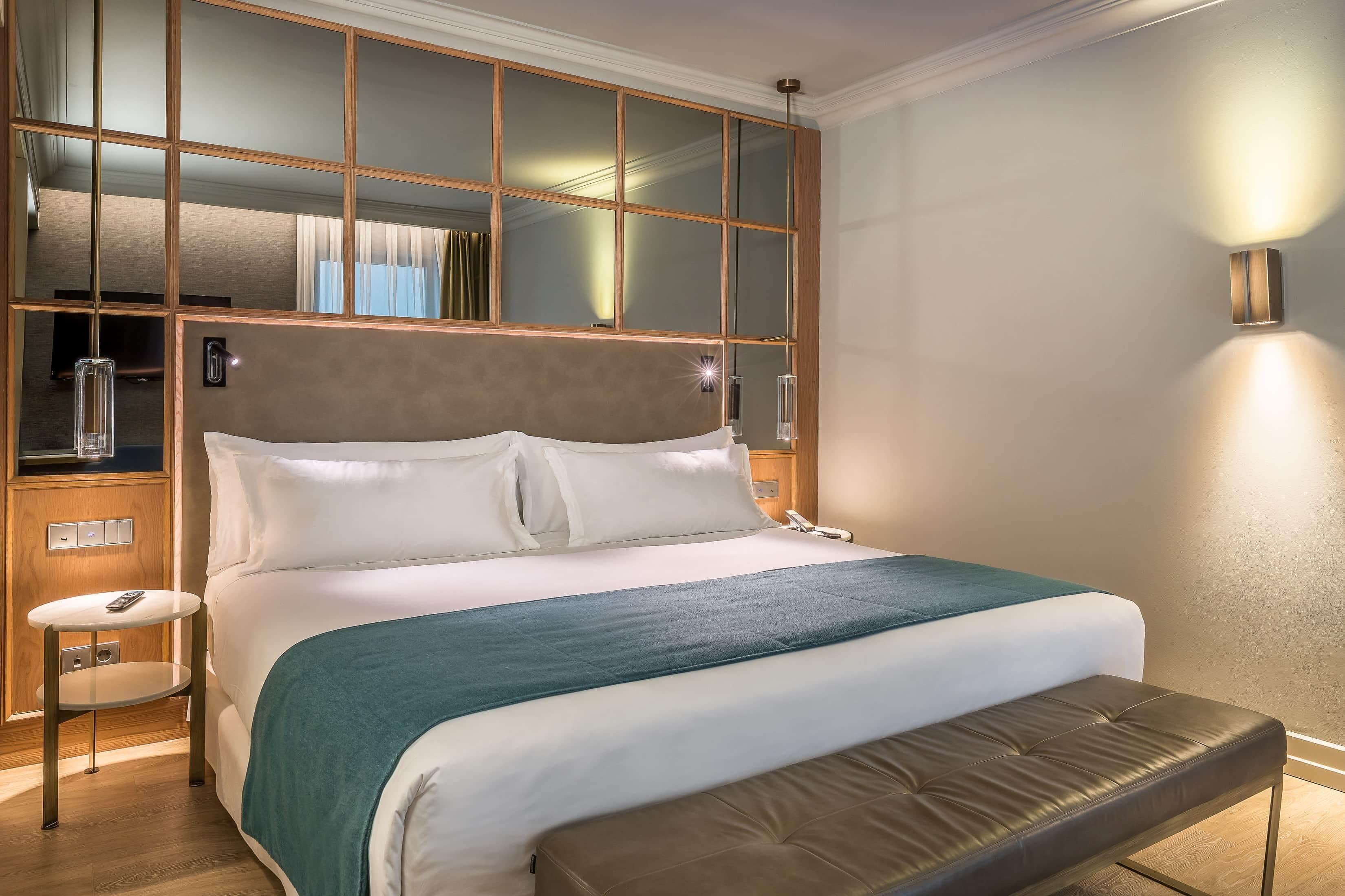 Una cama bien hecha con cabecera, mesitas de noche y un banco.
