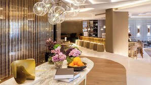 A modern hotel lobby with a marble reception desk, a bar area, and a seating area with sofas and chairs.