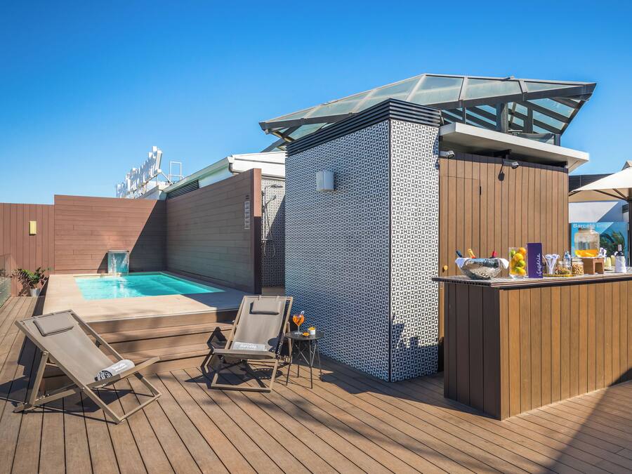 Un área de piscina en la azotea con un jacuzzi, sillones de descanso y un bar.