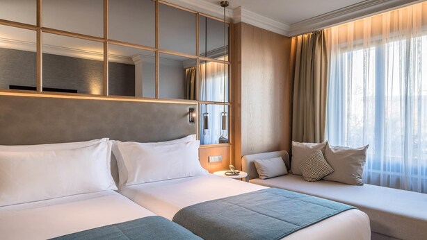 A hotel room with two beds, a large mirror, and a window with curtains. - Barceló Emperatriz (Madrid)