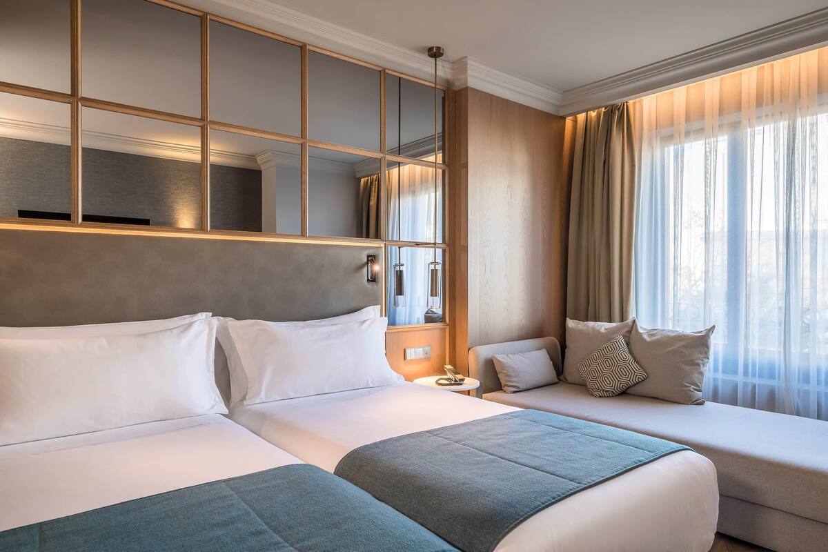 A hotel room with two beds, a large mirror, and a window with curtains.