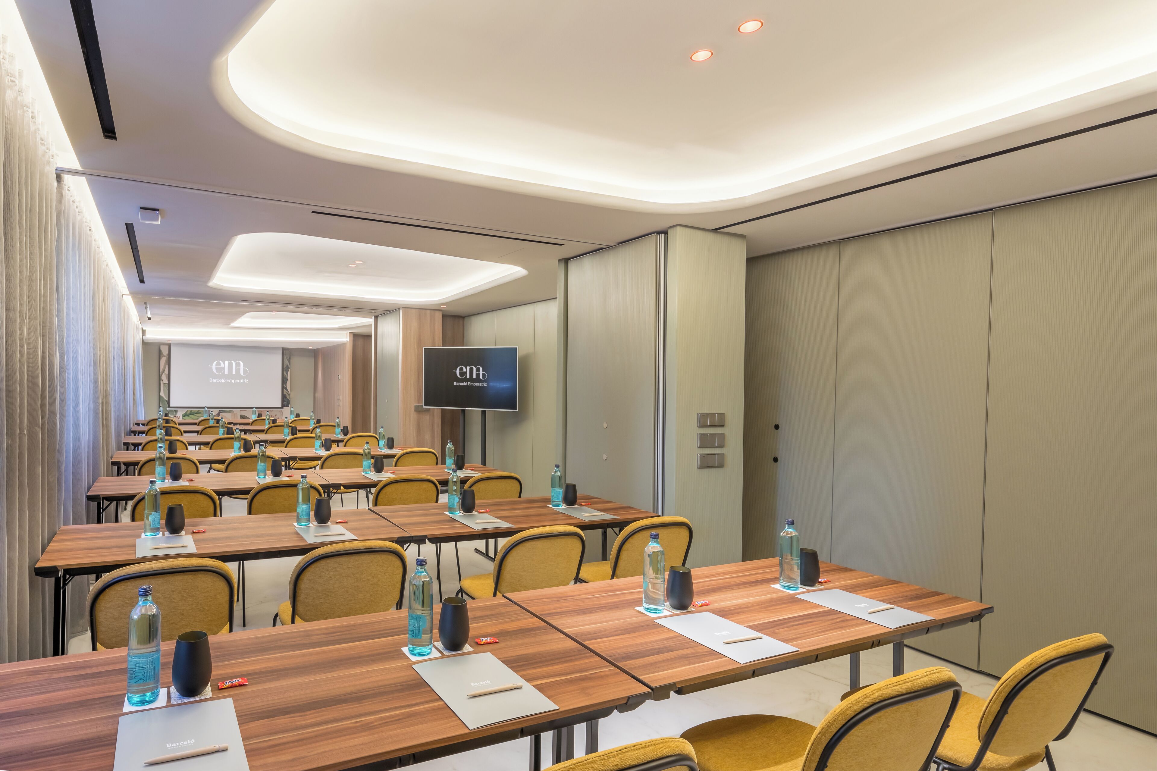 Un salón de conferencias con varias mesas, sillas y una pantalla grande.