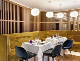 Un restaurante con una decoración moderna, que presenta una pared de listones de madera, iluminación colgante redonda y una zona de asientos con cabinas doradas.