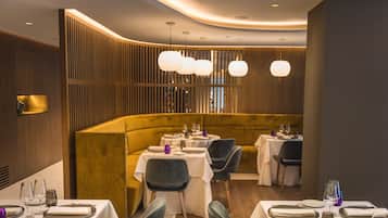 Un restaurante con una decoración moderna, que cuenta con una zona de asientos curva con mesas y sillas, iluminación ambiental y una pared decorativa de madera.