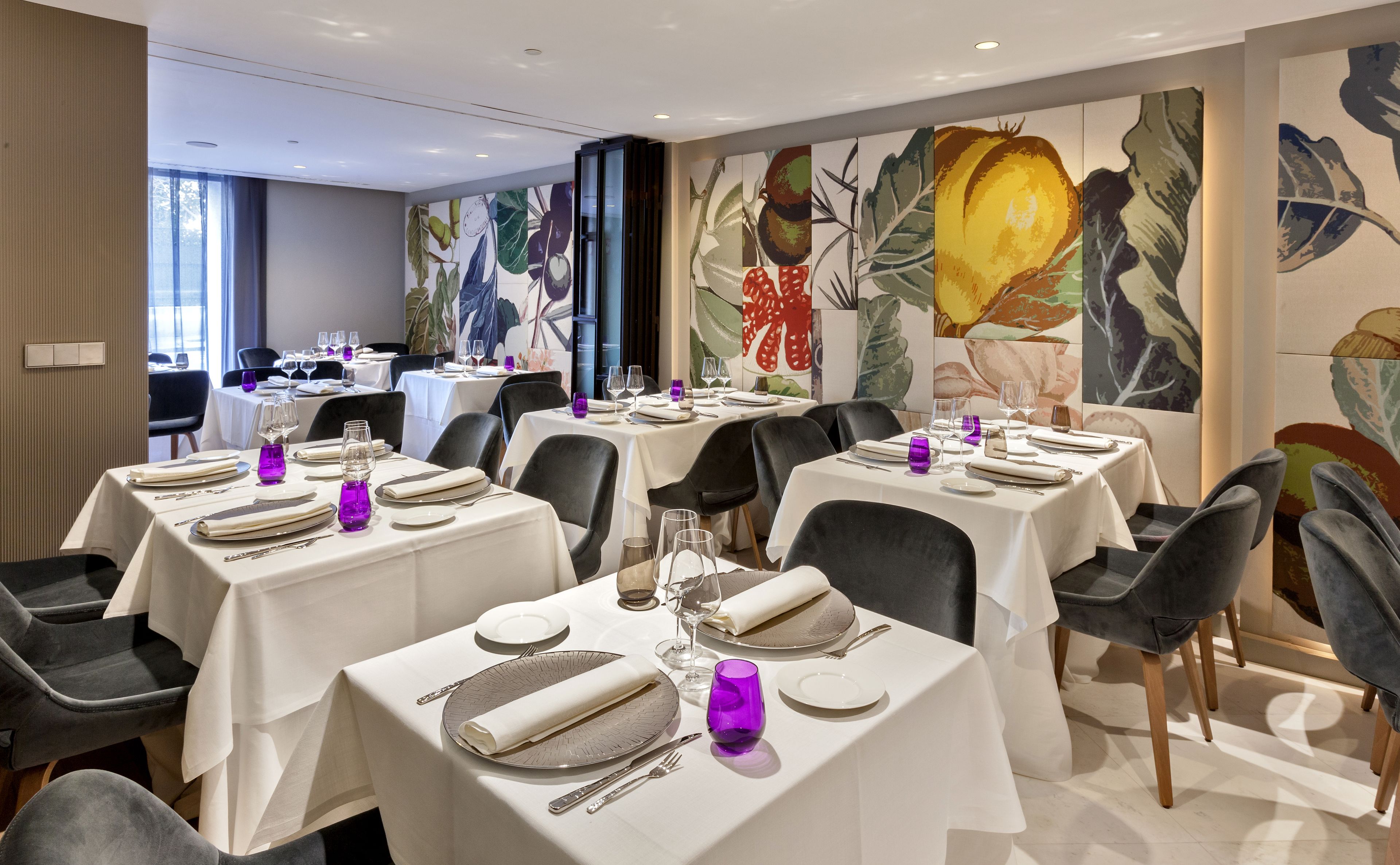 A restaurant with multiple tables set for dining, featuring white tablecloths and purple glassware.