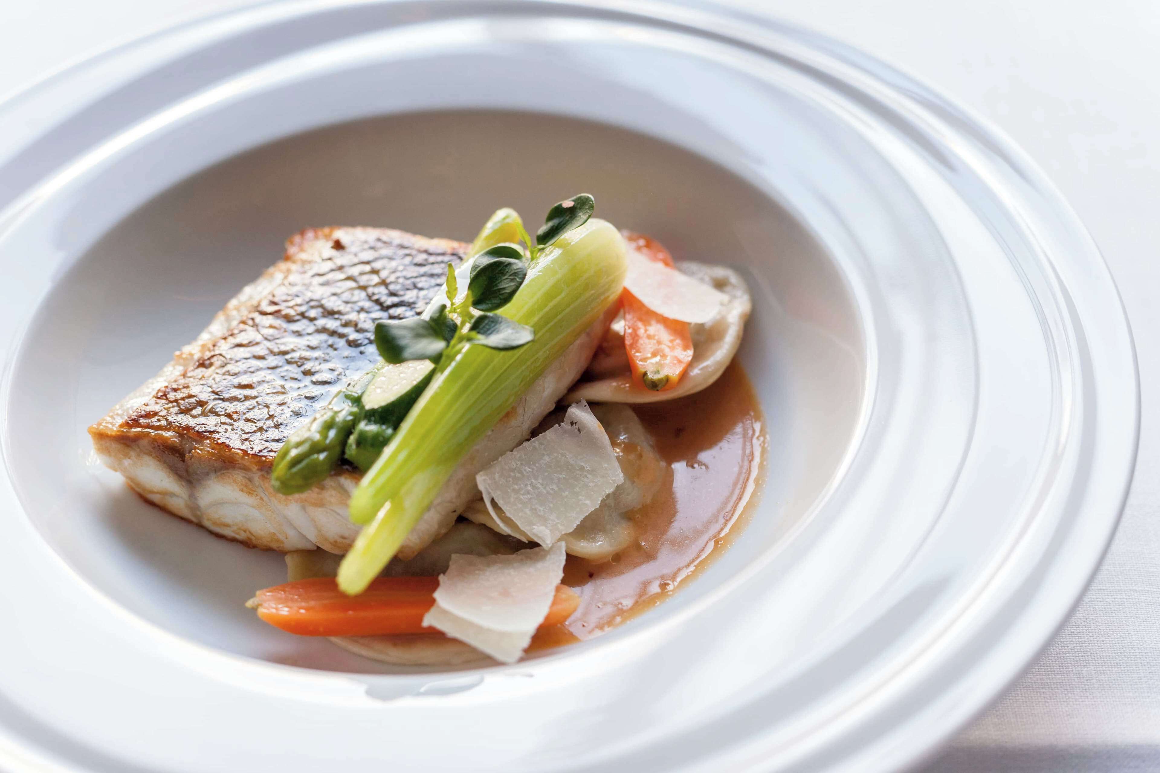 A dish with a piece of fish, vegetables, and a sauce in a white bowl.