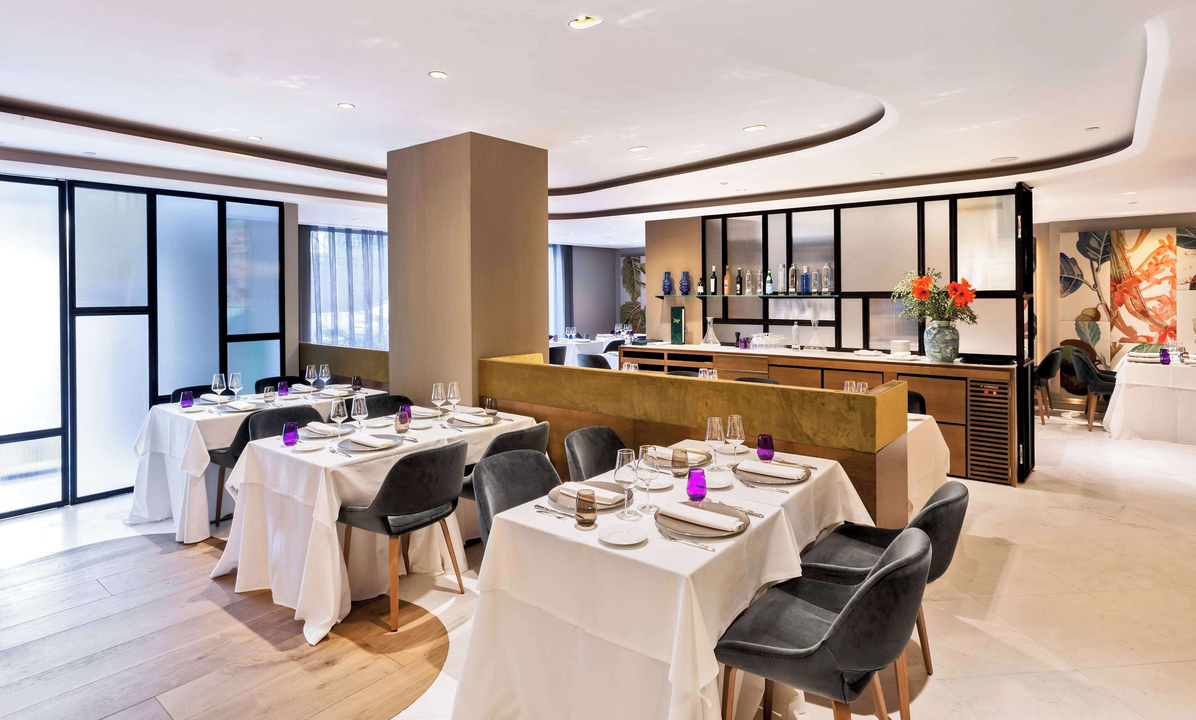 Een modern restaurant met gedekte tafels, een bar en grote ramen die voor natuurlijk licht zorgen.