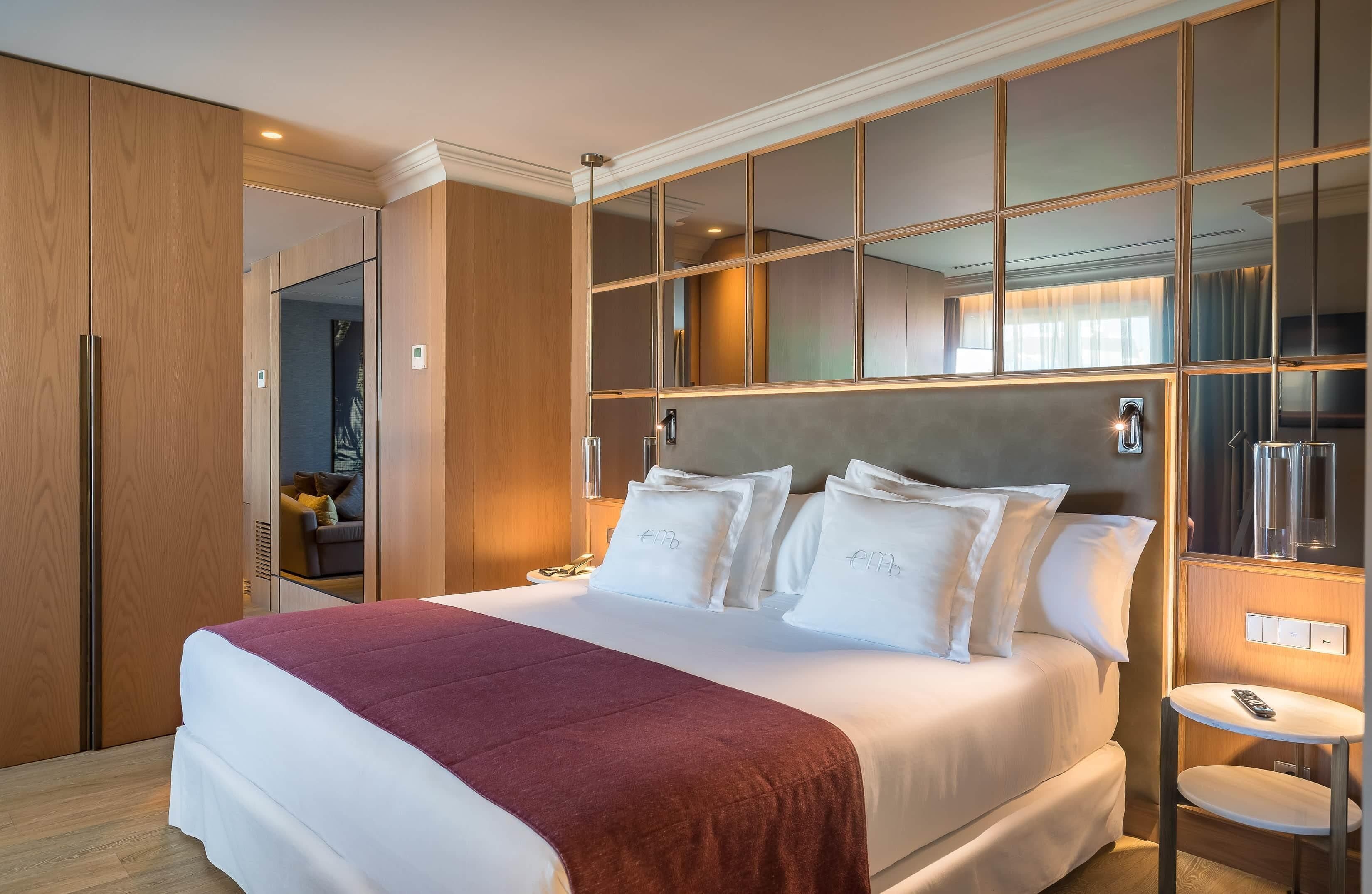 Una habitación de hotel con una cama grande, un armario de madera, un espejo y una mesita con un control remoto.