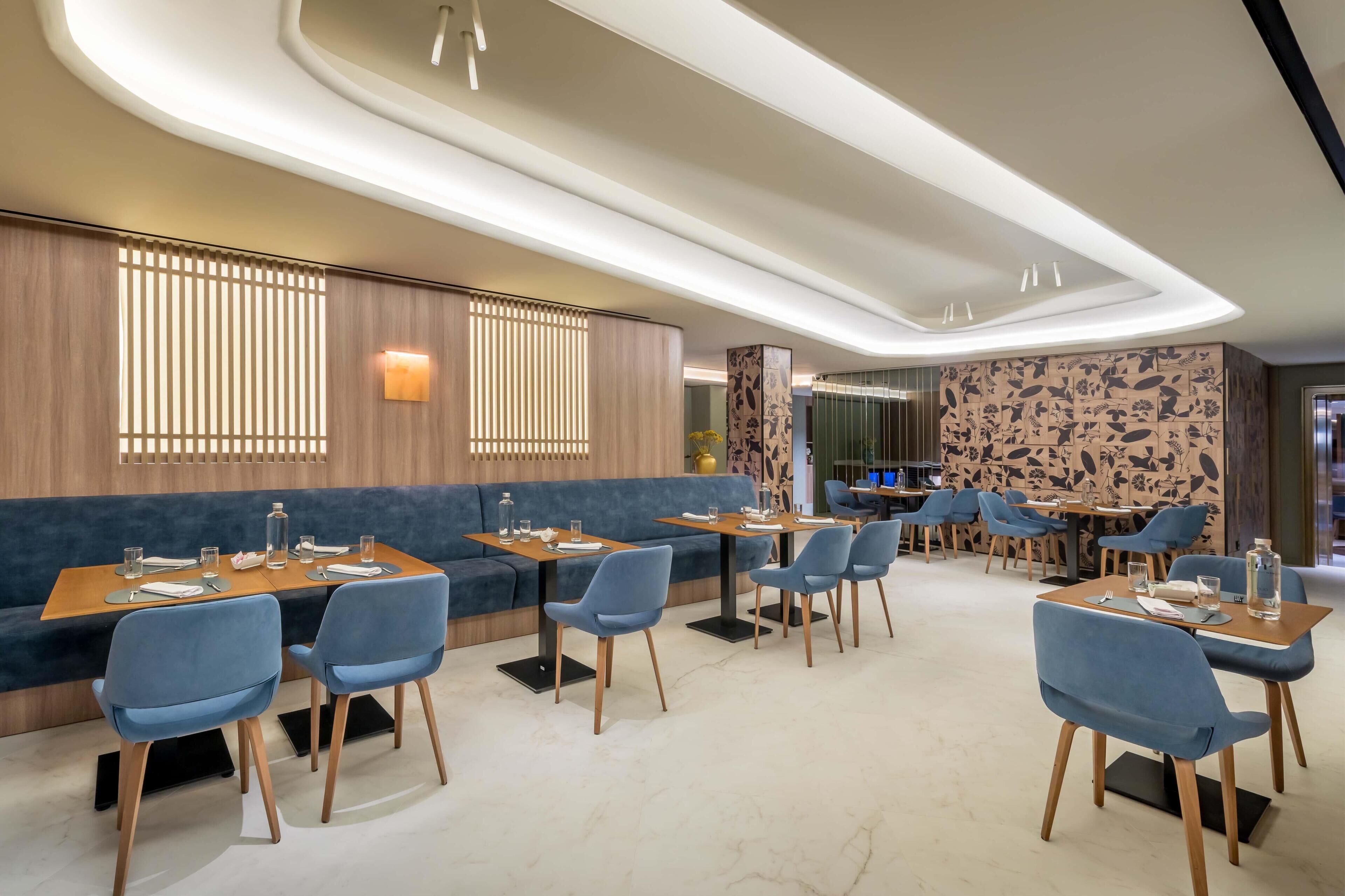 Un restaurante moderno con asientos azules, mesas de madera y paneles decorativos en la pared.