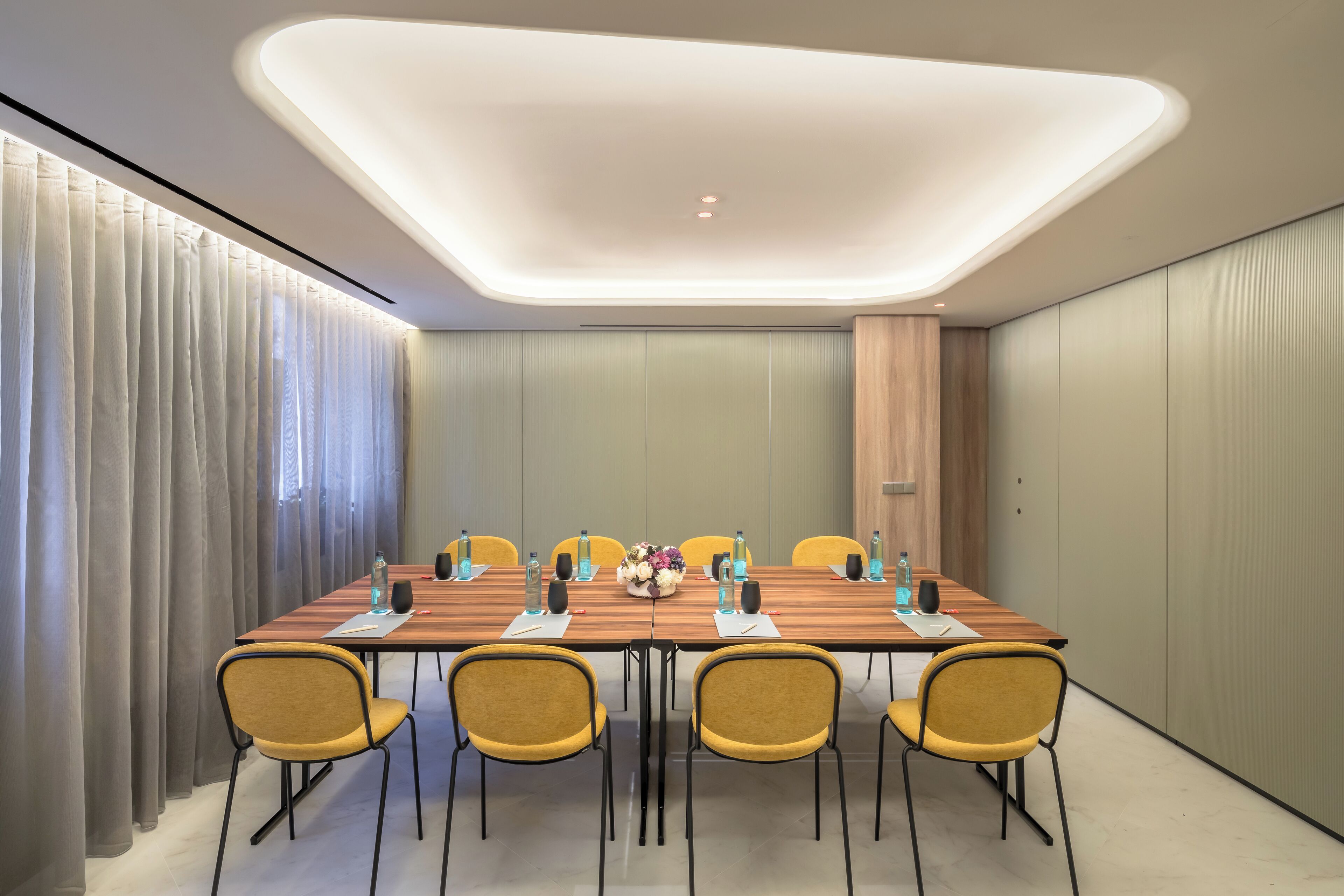Une salle de conférence avec une longue table, des chaises jaunes et un luminaire moderne au plafond.