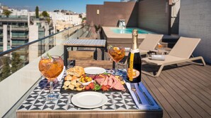 A rooftop terrace with a table set for a meal, a bottle of champagne, and a glass of wine.