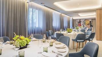 A modern dining area with round tables, blue chairs, and a large window with curtains.