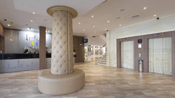 A spacious lobby with a central column, a reception desk, and a staircase leading to upper floors. - Hotel Puerta de Toledo (Madrid)
