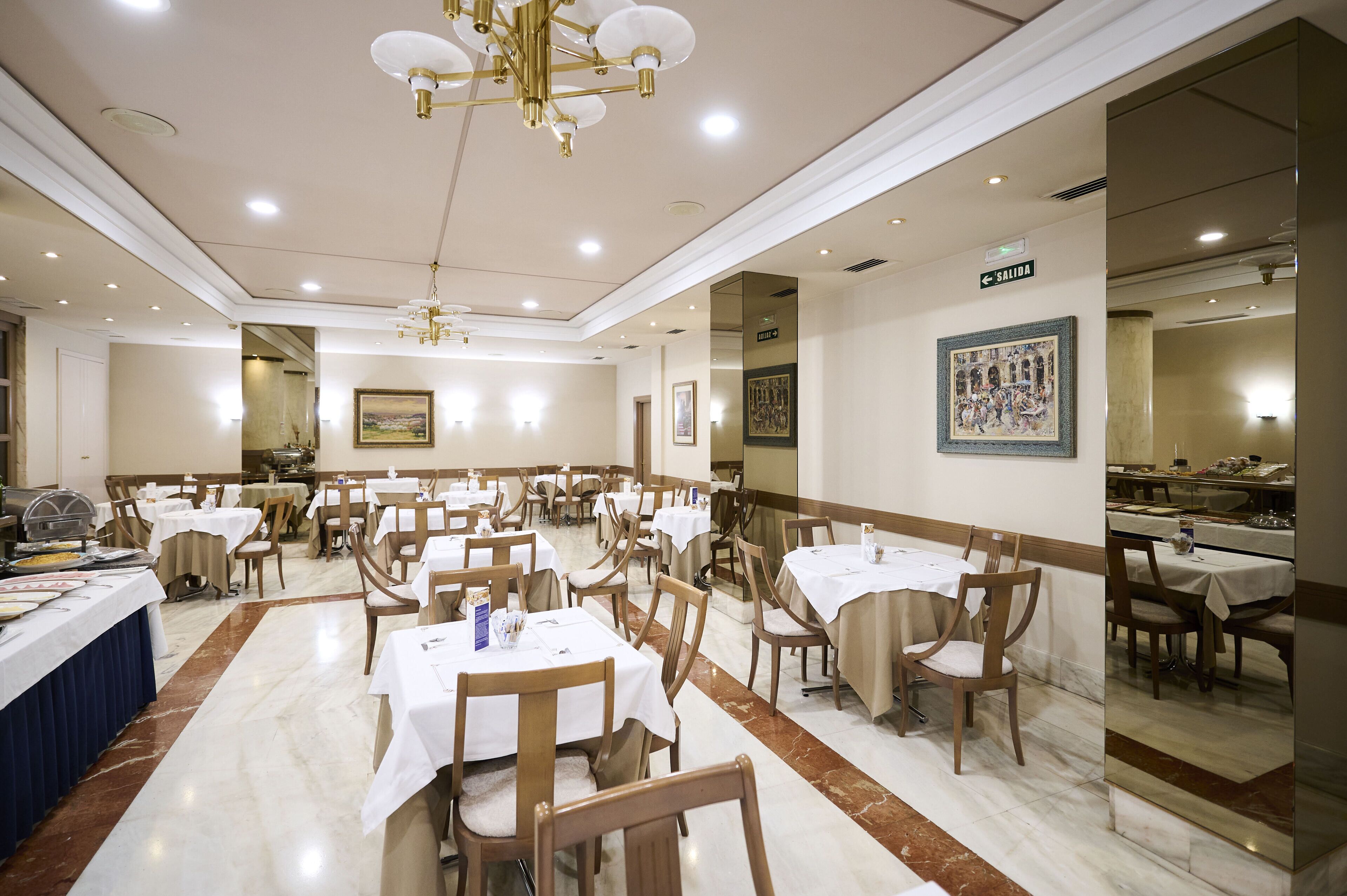 A spacious dining area with multiple tables and chairs, a chandelier, and a sign indicating the exit.