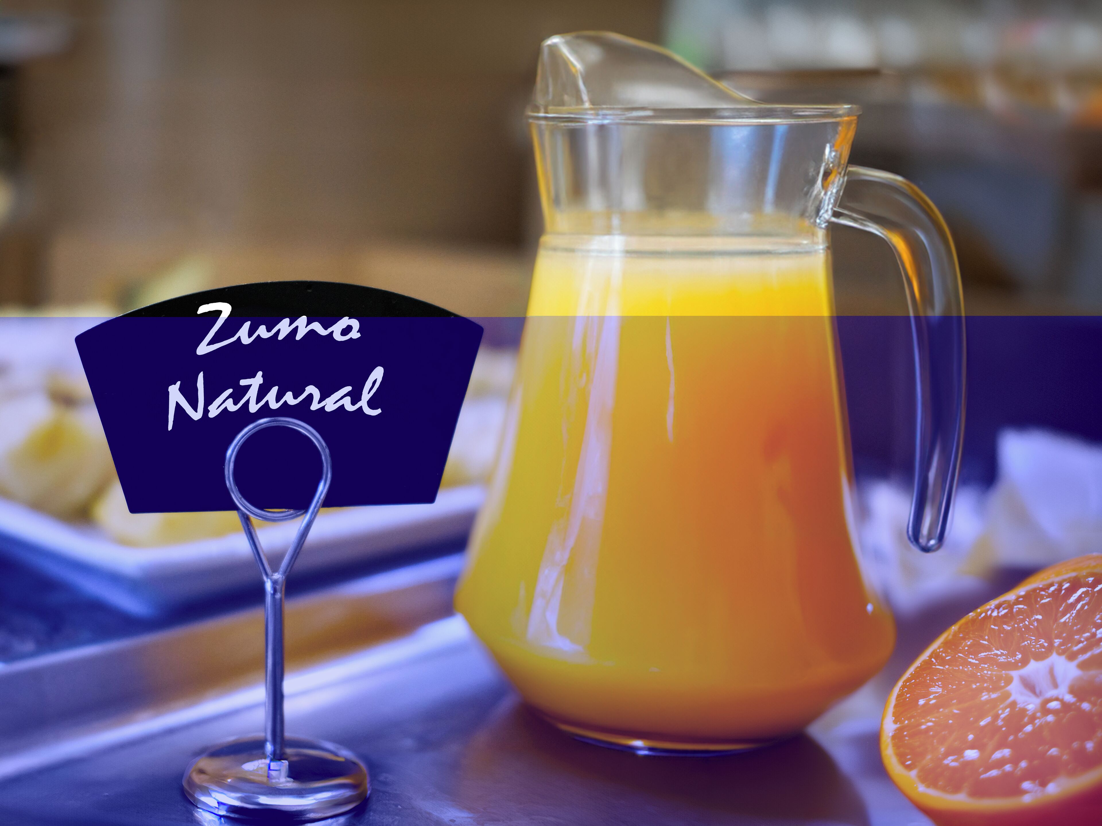 Un jarro de vidrio con jugo de naranja y una etiqueta que dice "Zuma Natural" sobre una mesa.