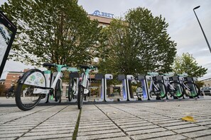 Una hilera de bicicletas eléctricas estacionadas en un área designada, con un edificio identificado como "ALBRET" al fondo.