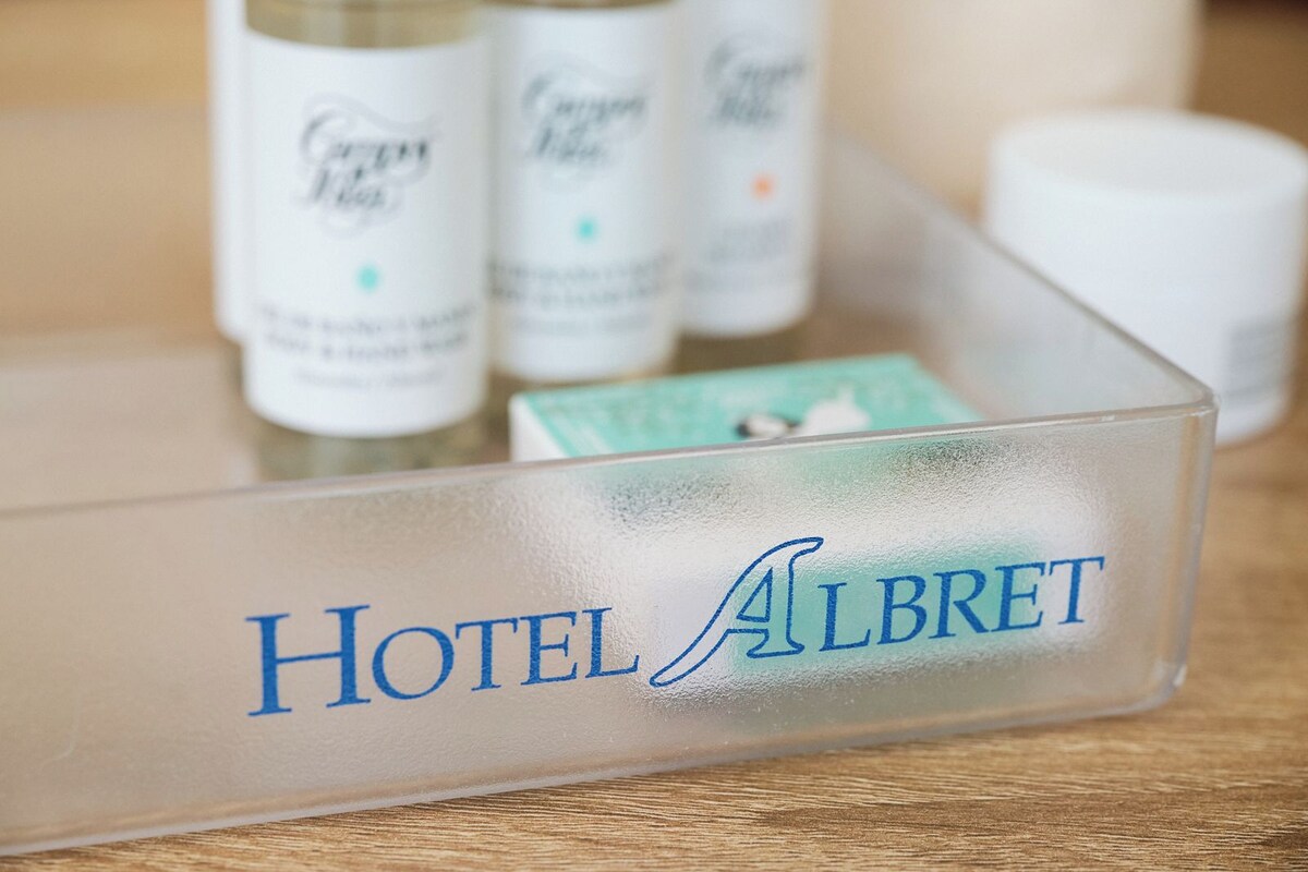 Un récipient transparent en plastique, portant l’étiquette « Hôtel Albrecht », et contenant divers articles de toilette.