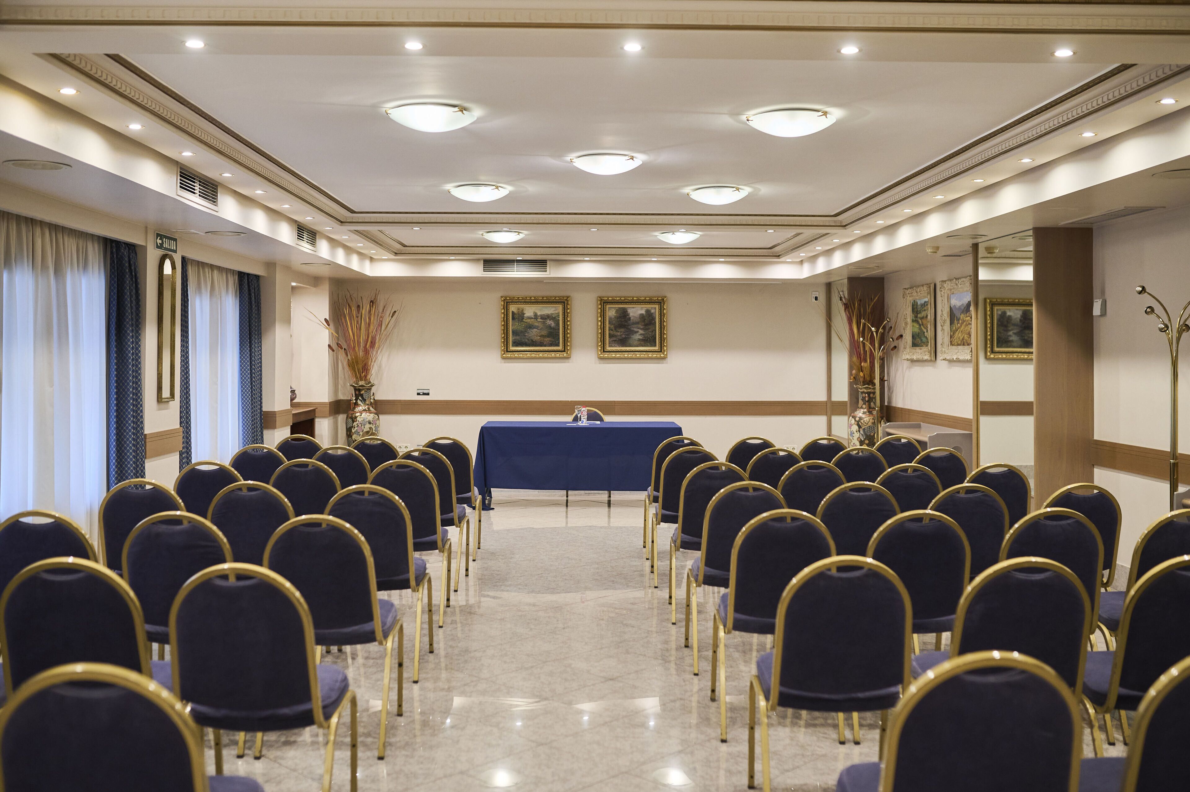 A conference room with rows of chairs, a table with a blue cloth, and framed pictures on the walls.
