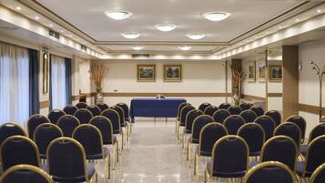 A conference room with rows of chairs, a table with a blue cloth, and framed pictures on the walls.
