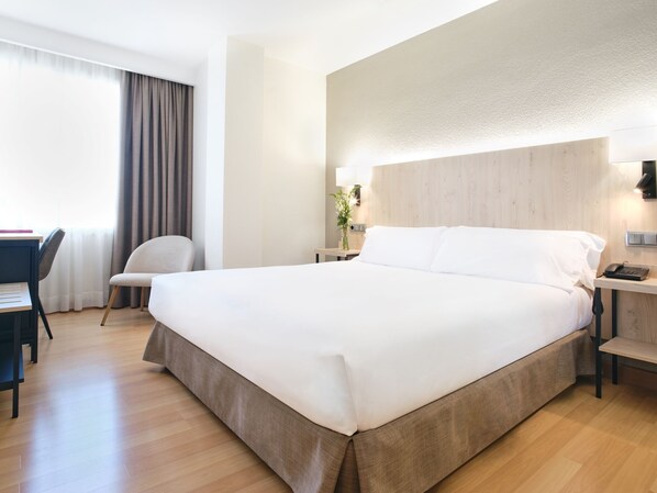 Habitación de hotel con una cama grande, un escritorio con silla, una lámpara y una mesita de noche con teléfono.