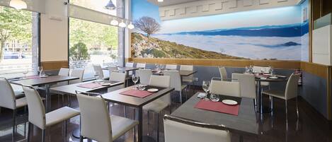 A restaurant with multiple tables and chairs, large windows, and a mural of a landscape.