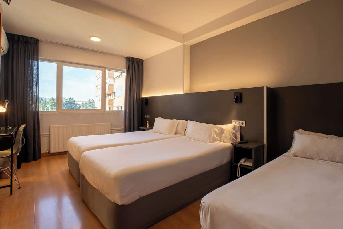 Hotellihuone, jossa on kaksi sänkyä, työpöytä ja tuoli.