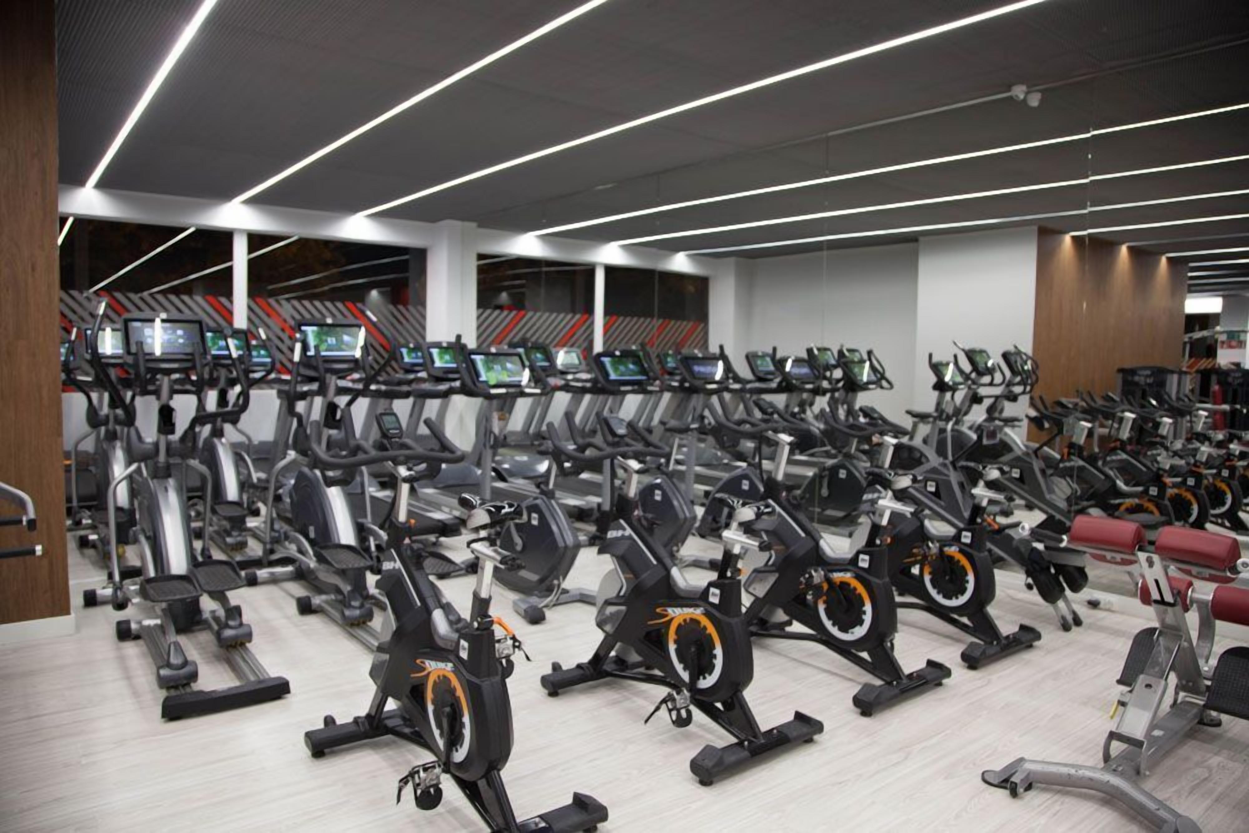 Un gimnasio con varias bicicletas estáticas y cintas de correr, dispuestas en filas.
